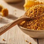 Bunte Blütenpollen-Kügelchen in Gelb, Orange und Braun in einem Holzlöffel und einer Schale auf hellem Holz