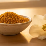 Goldene Blütenpollen in einer Schale neben einer blühenden Blume mit sichtbarem Pollen auf hellem Holz