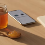 Manuka-Honig-Glas, Löffel, Smartphone mit unscharfer Bewertungsanzeige und Notizbuch auf hellem Tisch