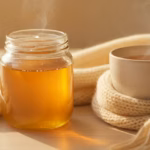 Manuka-Honig-Glas, eine Tasse lauwarmer Tee und ein weicher Schal auf hellem Tisch