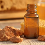 Rohes rotbraunes Propolis-Kittharz, ein Tropffläschchen mit Propolis-Tinktur und ein Stück Bienenwachs vor Honigwaben im warmen Licht