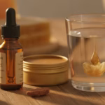 Verschiedene Propolis-Produkte – Tropffläschchen, Salbendose und ein Glas Wasser mit Tropfen, im Hintergrund rohes Propolis und Honigwabe